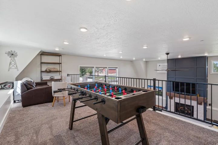 Carpeted loft area with recessed lighting, black metal railing overlooking the lower level, and a ceiling fan