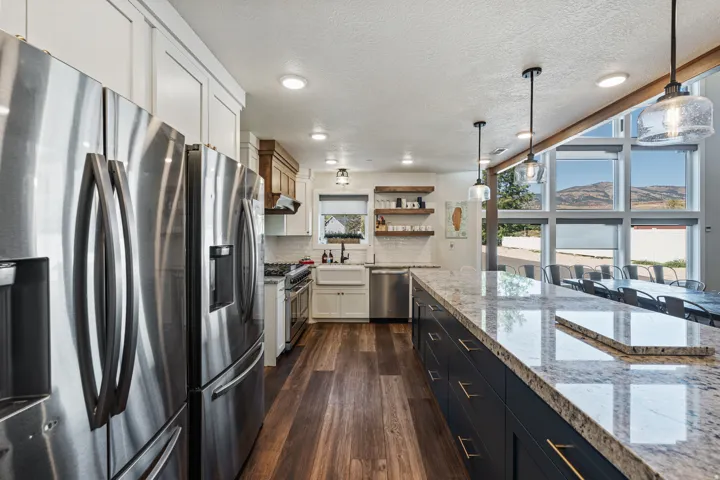 Gourmet kitchen featuring stainless steel appliances, wood-finish flooring, a large island with a stone countertop, pendant lighting, and expansive windows