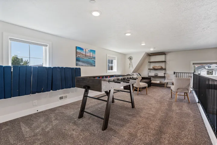 Carpeted upper-level space featuring recessed lighting, multiple windows, a sloped ceiling, and an open metal railing