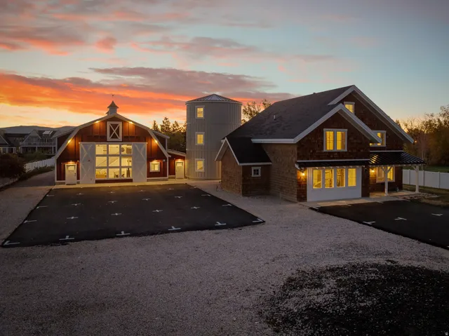 Multiple structures with shingle siding and dark roofs, including a barn-style building with large glass doors and a silo-style structure with multiple windows