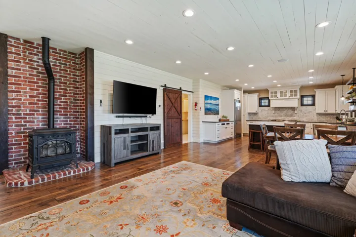 Wood-finish flooring throughout, brick accent wall with a wood-burning stove, white shiplap walls, recessed lighting, and white cabinetry with dark countertops