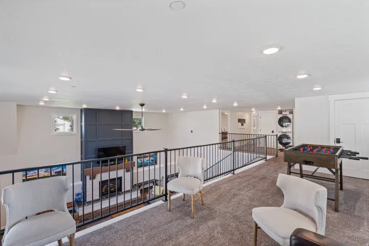 Expansive loft with recessed lighting, dark metal railings, and a view of a living space featuring a fireplace with a wood mantel and a paneled accent wall