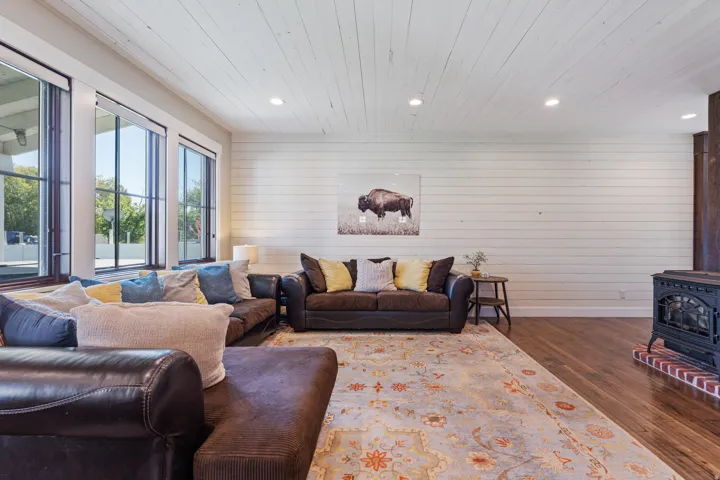 Hardwood flooring, shiplap wall finishes, wood-paneled ceiling, recessed lighting, and a cast iron wood-burning stove with brick base