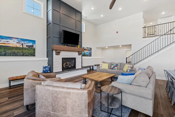 Two-story living area featuring a fireplace with a wood mantel, a paneled accent wall, a staircase with metal railings, and wood-finish flooring