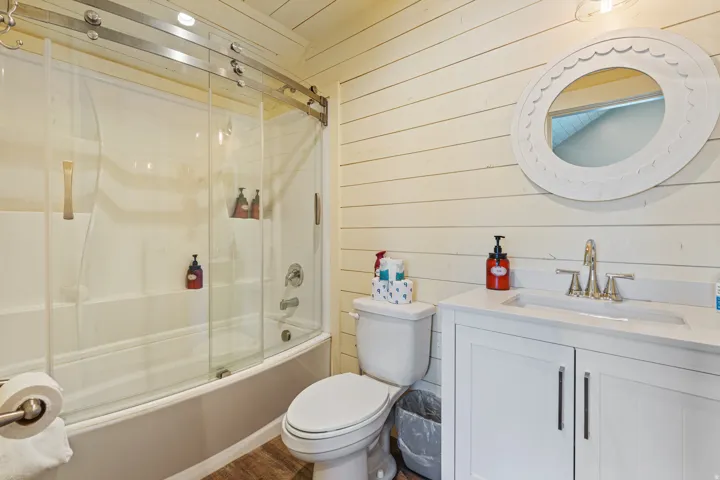 Full bathroom featuring a single vanity, integrated sink, wood-finish flooring, and a shower-tub combination with a glass enclosure
