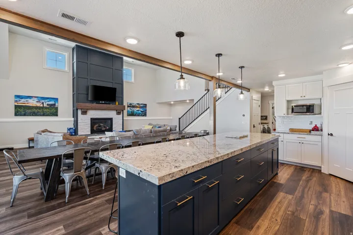 Expansive open concept living area featuring wood-finish flooring, a contemporary fireplace with a decorative mantel, and a spacious kitchen island with a light-toned countertop