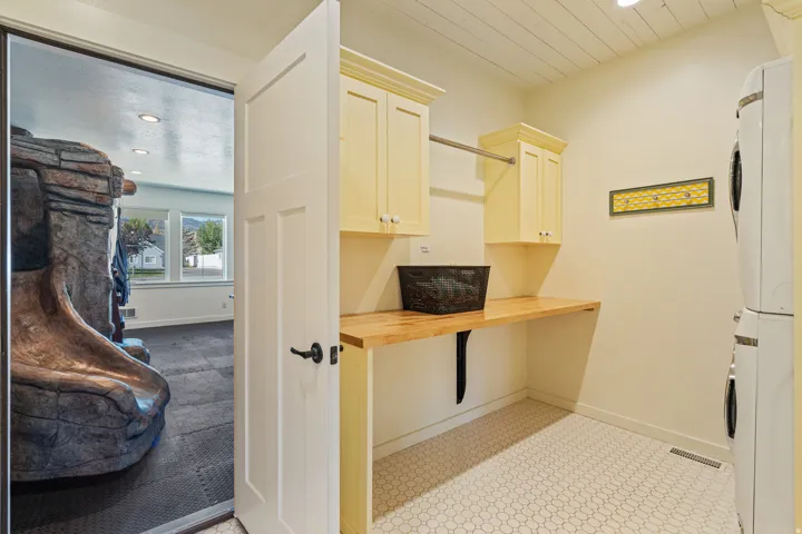 Laundry area featuring white honeycomb tile flooring, light-colored upper cabinetry, and wood-finish countertops