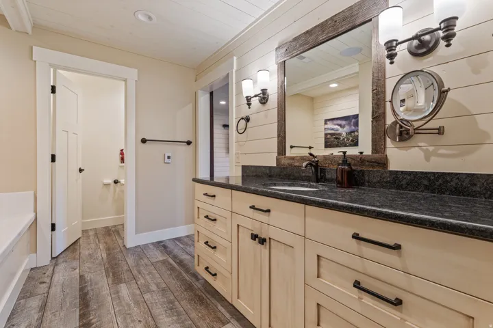 Wood-finish flooring, stone countertop vanity with integrated sink, rectangular mirror with rustic wood frame, and dual wall-mounted light fixtures
