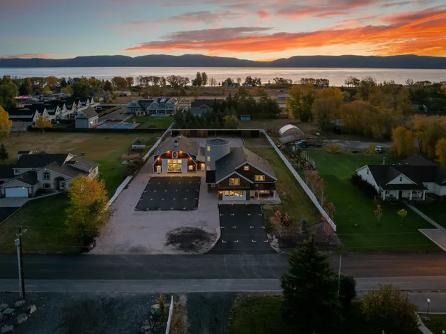 Expansive property featuring two distinct structures, a substantial driveway, mature trees, and a white perimeter fence