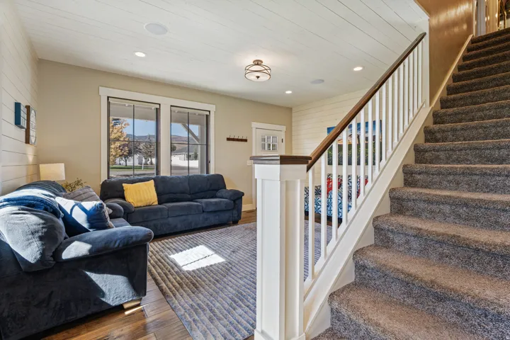 Shiplap accent wall, wood-finish flooring, two large windows, recessed ceiling lighting, and a staircase with a white balustrade and wood handrail