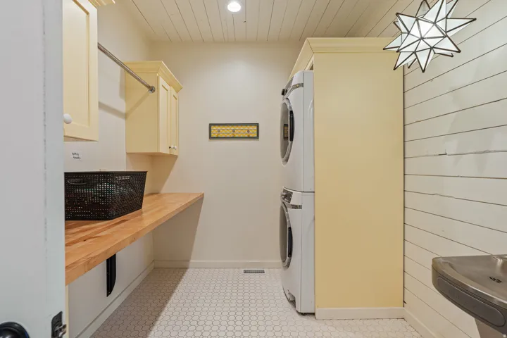 Stacked washer and dryer, wood-finish countertop, upper cabinetry, hexagon tile flooring, and shiplap wall detail