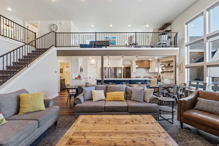 Two-story living area with high ceilings, large windows, an open kitchen with a central island, and a second-level balcony