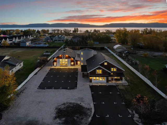 Coastal scenery backdrop, main residence with covered porch, separate red barn-style structure, paved driveways, and white picket fencing