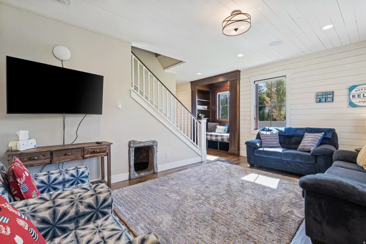 White shiplap accent wall, built-in window seat with storage, wood-finish flooring, staircase with white railings, and a decorative ceiling light fixture