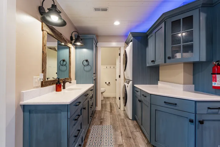 Extended vanity with a rectangular sink, dual wall sconces, wood-finish flooring, stacked laundry appliances, and custom blue cabinetry