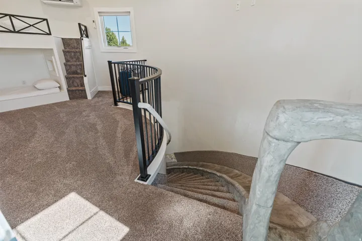 Carpeted loft area featuring a built-in bunk bed structure, a curved metal railing, and a window with exterior views
