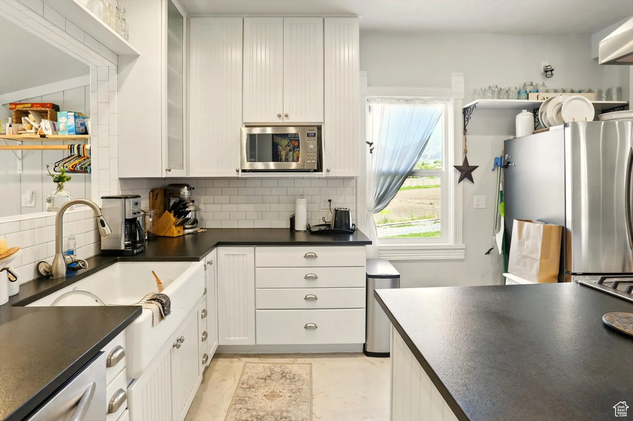 Kitchen with appliances with stainless steel finishes, dark countertops, tasteful backsplash, white cabinetry, and glass insert cabinets