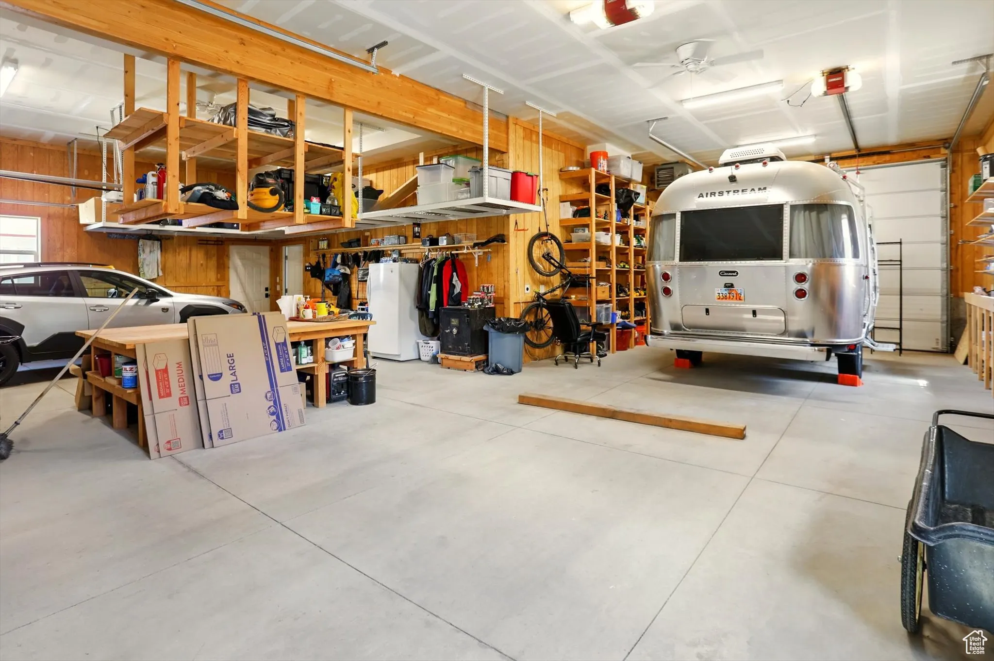 Garage featuring freestanding refrigerator, wooden walls, and ceiling fan