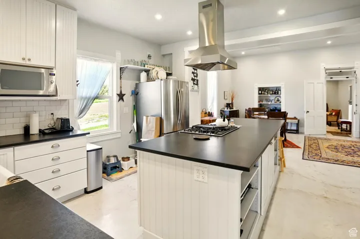 Kitchen featuring stainless steel appliances, dark countertops, island range hood, a center island, and tasteful backsplash