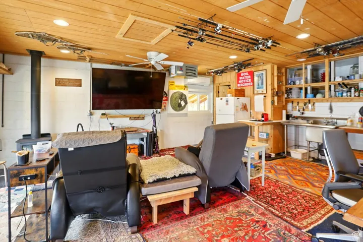 Office area with ceiling fan, a wood stove, wooden ceiling, and concrete block wall