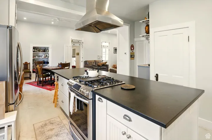 Kitchen with appliances with stainless steel finishes, island exhaust hood, dark countertops, white cabinets, and a ceiling fan