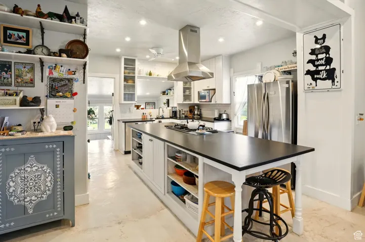 Kitchen with island exhaust hood, open shelves, appliances with stainless steel finishes, a ceiling fan, and dark countertops
