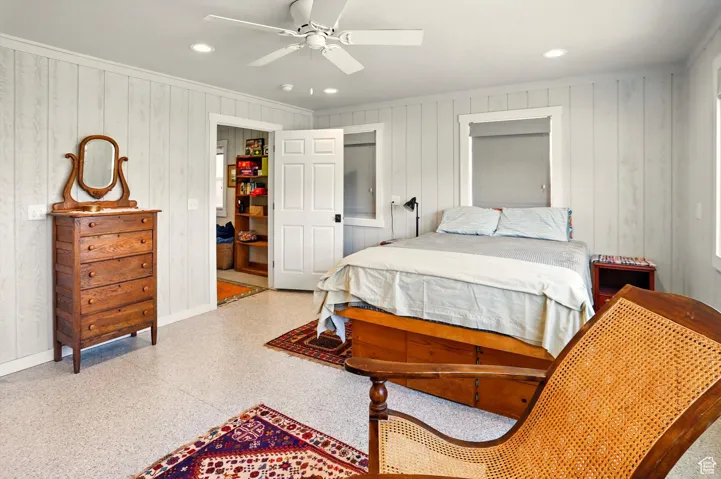Bedroom with speckle patterned floor, baseboards, crown molding, wood walls, and ceiling fan