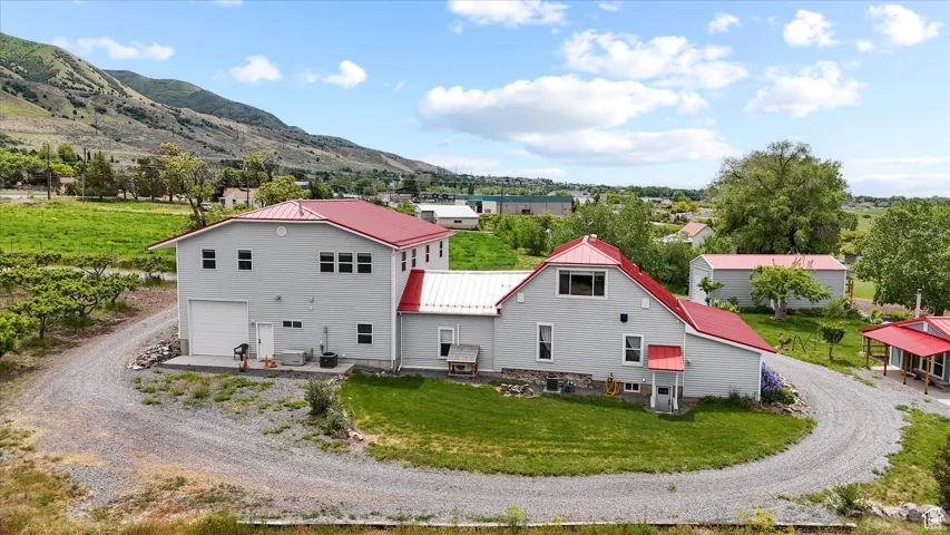 Back of property with dirt driveway, a mountain view, metal roof, a lawn, and a garage