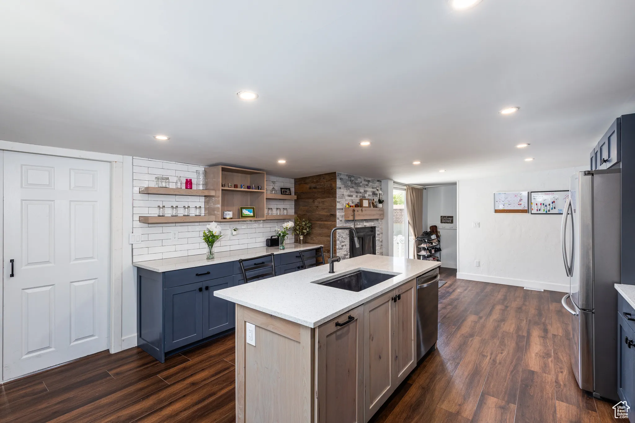 Kitchen featuring a sink, stainless steel appliances, a fireplace, an island with sink, and dark wood-style flooring