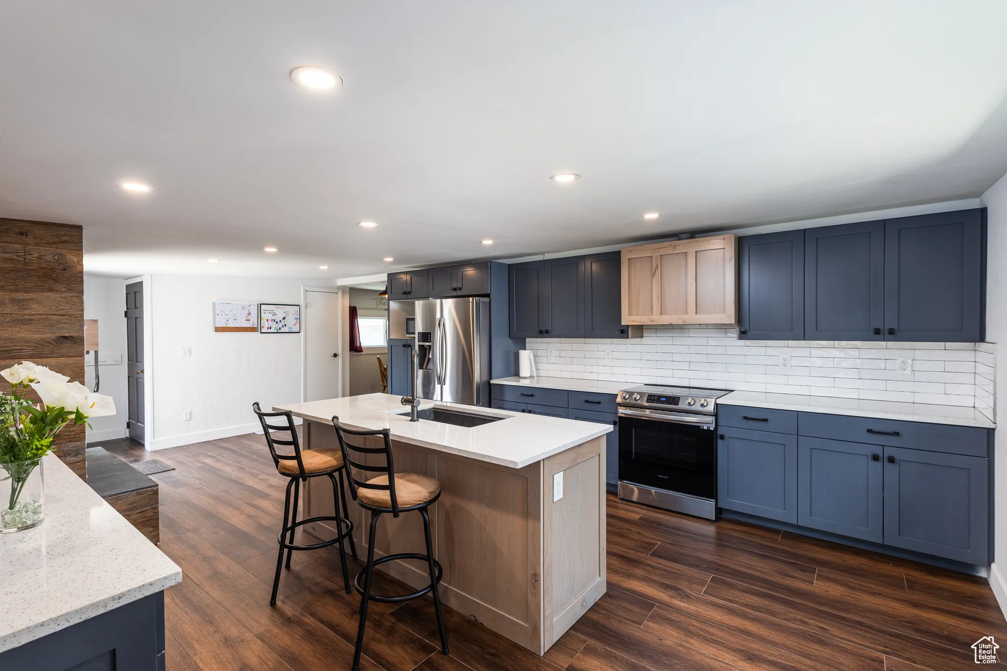Kitchen with appliances with stainless steel finishes, a kitchen breakfast bar, decorative backsplash, dark wood-style floors, and a center island with sink