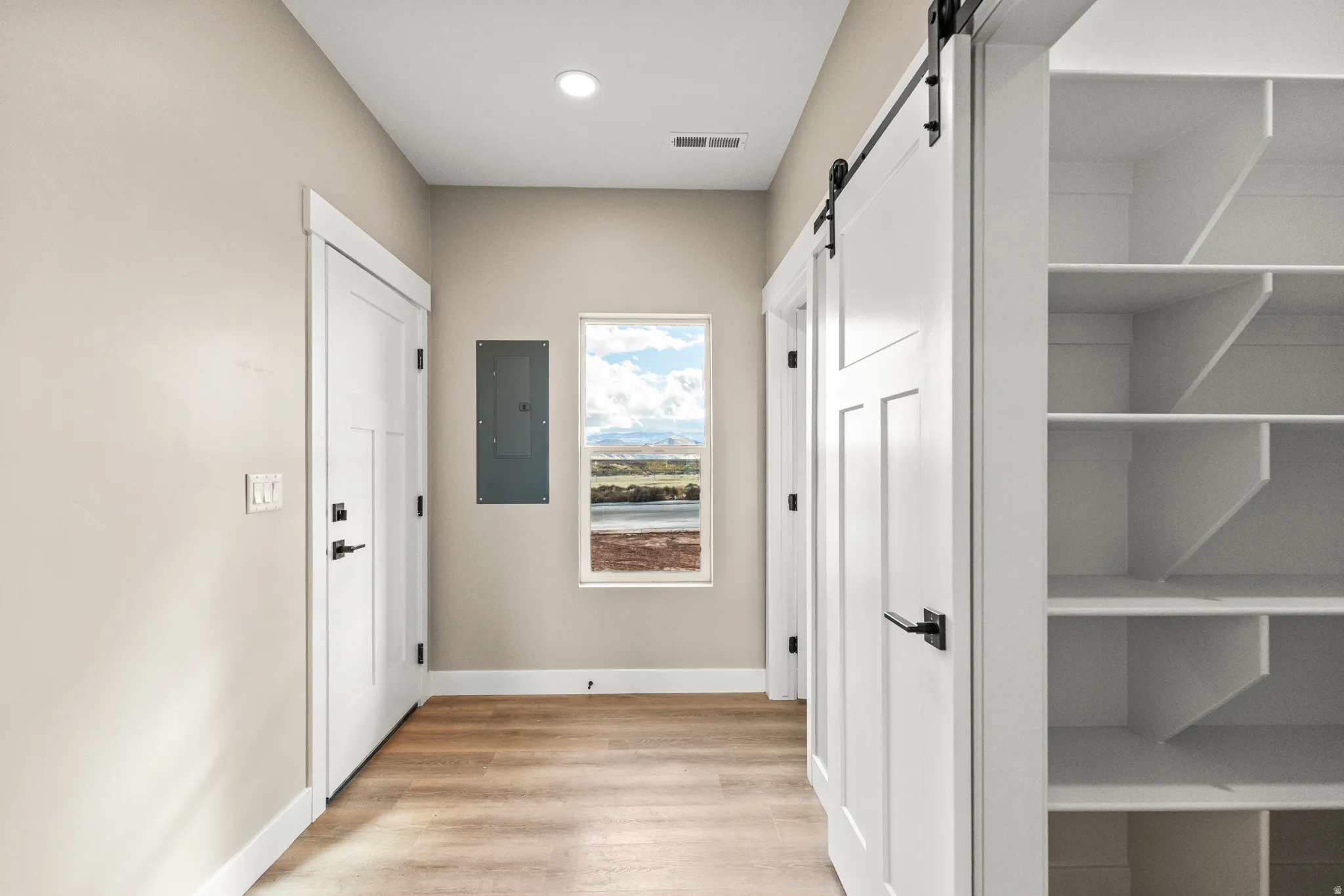 Hall with a barn door, light wood-style floors, and electric panel