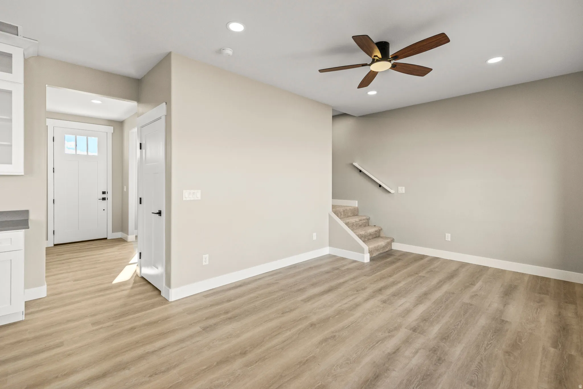 Unfurnished living room with stairway, light wood-type flooring, ceiling fan, and recessed lighting