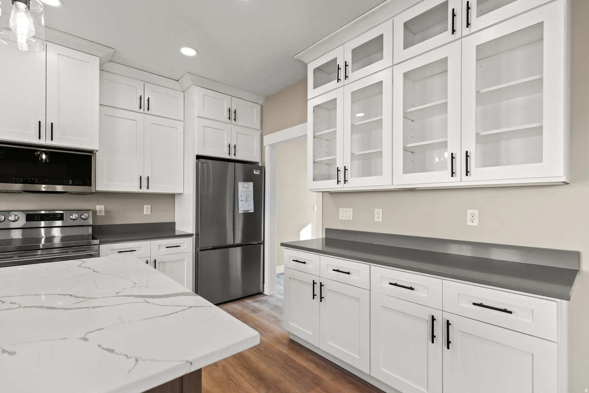 Kitchen with white cabinets, stainless steel appliances, dark wood finished floors, dark stone countertops, and recessed lighting
