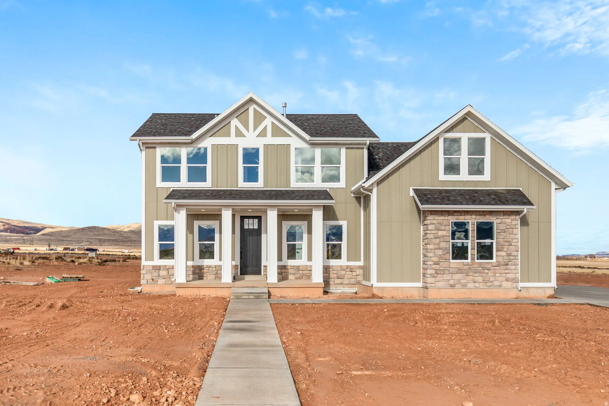 Craftsman inspired home featuring stone siding, covered porch, board and batten siding, and roof with shingles