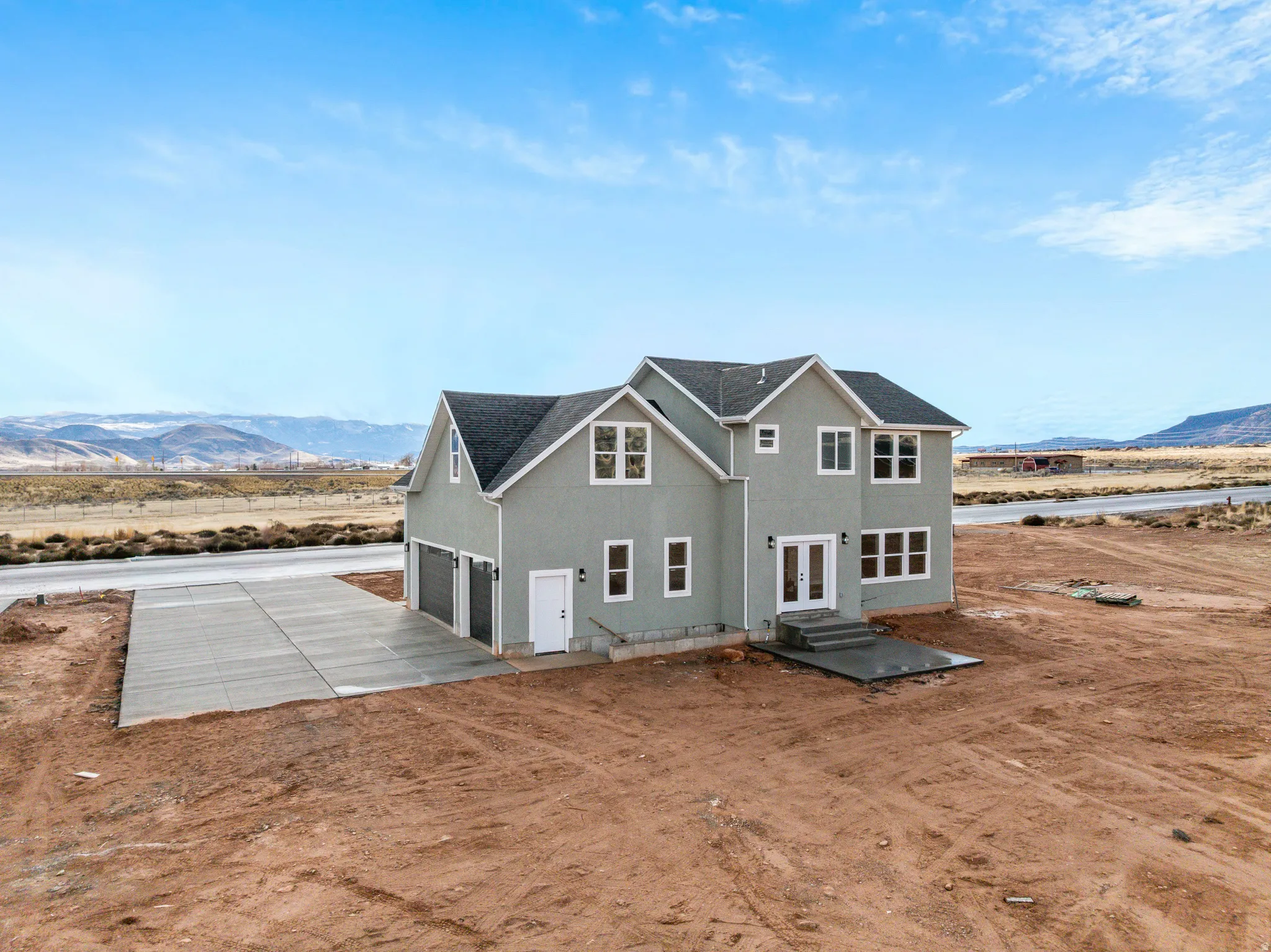 View of front of home featuring a mountain view, dirt driveway, stucco siding, an attached garage, and french doors