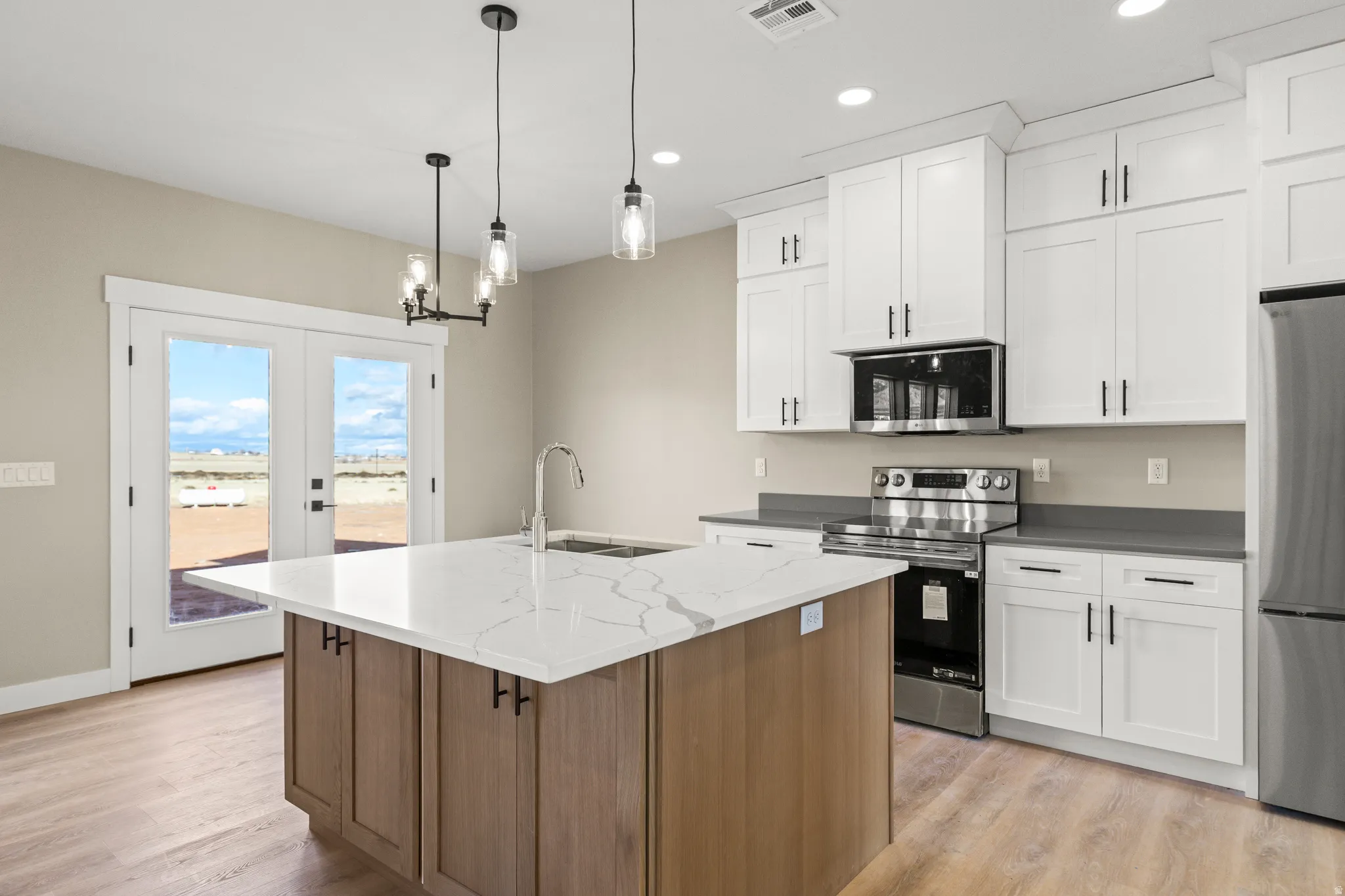 Kitchen featuring appliances with stainless steel finishes, french doors, pendant lighting, a kitchen island with sink, and light wood-type flooring