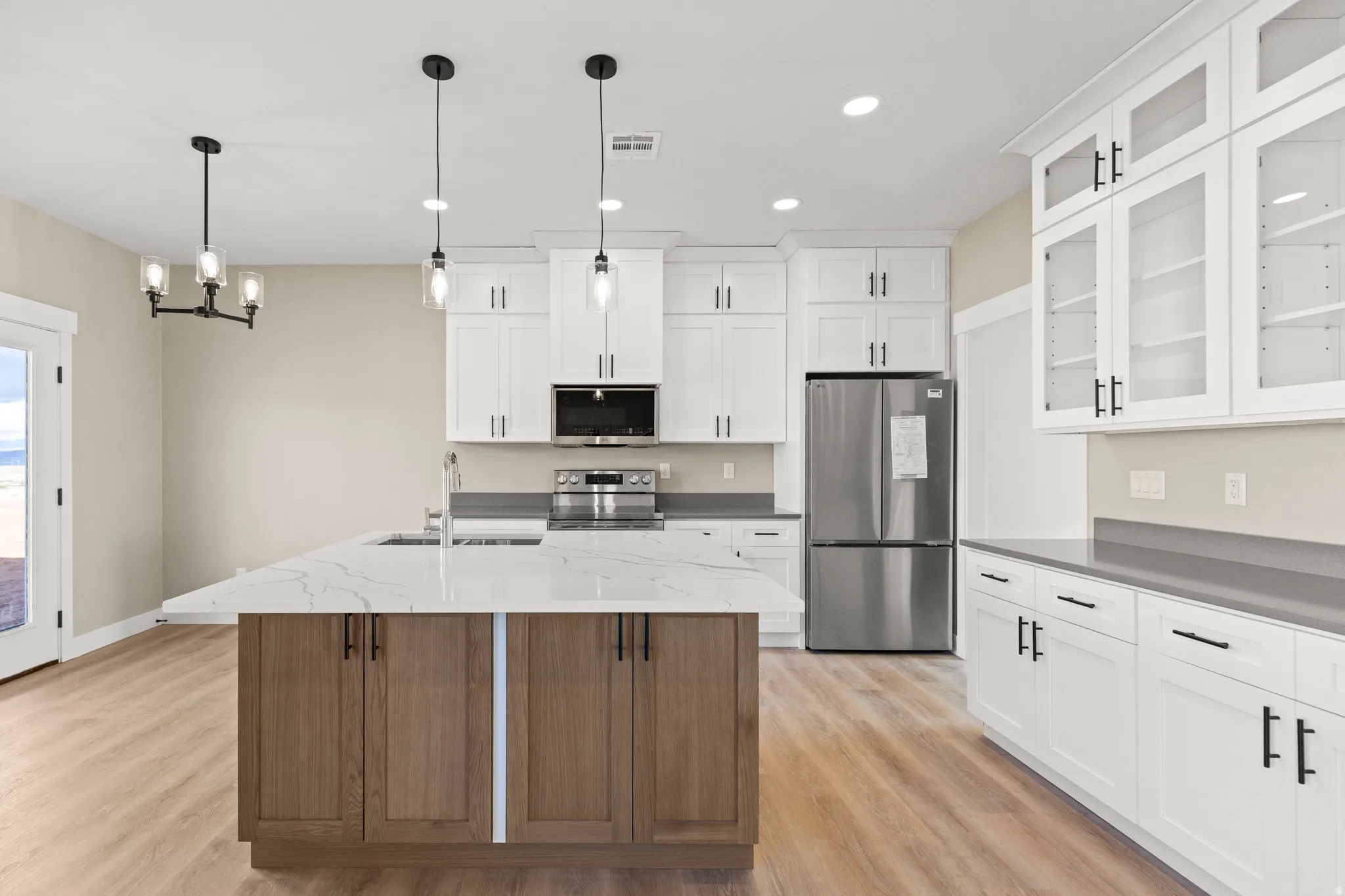 Kitchen with appliances with stainless steel finishes, glass insert cabinets, white cabinets, a center island with sink, and pendant lighting