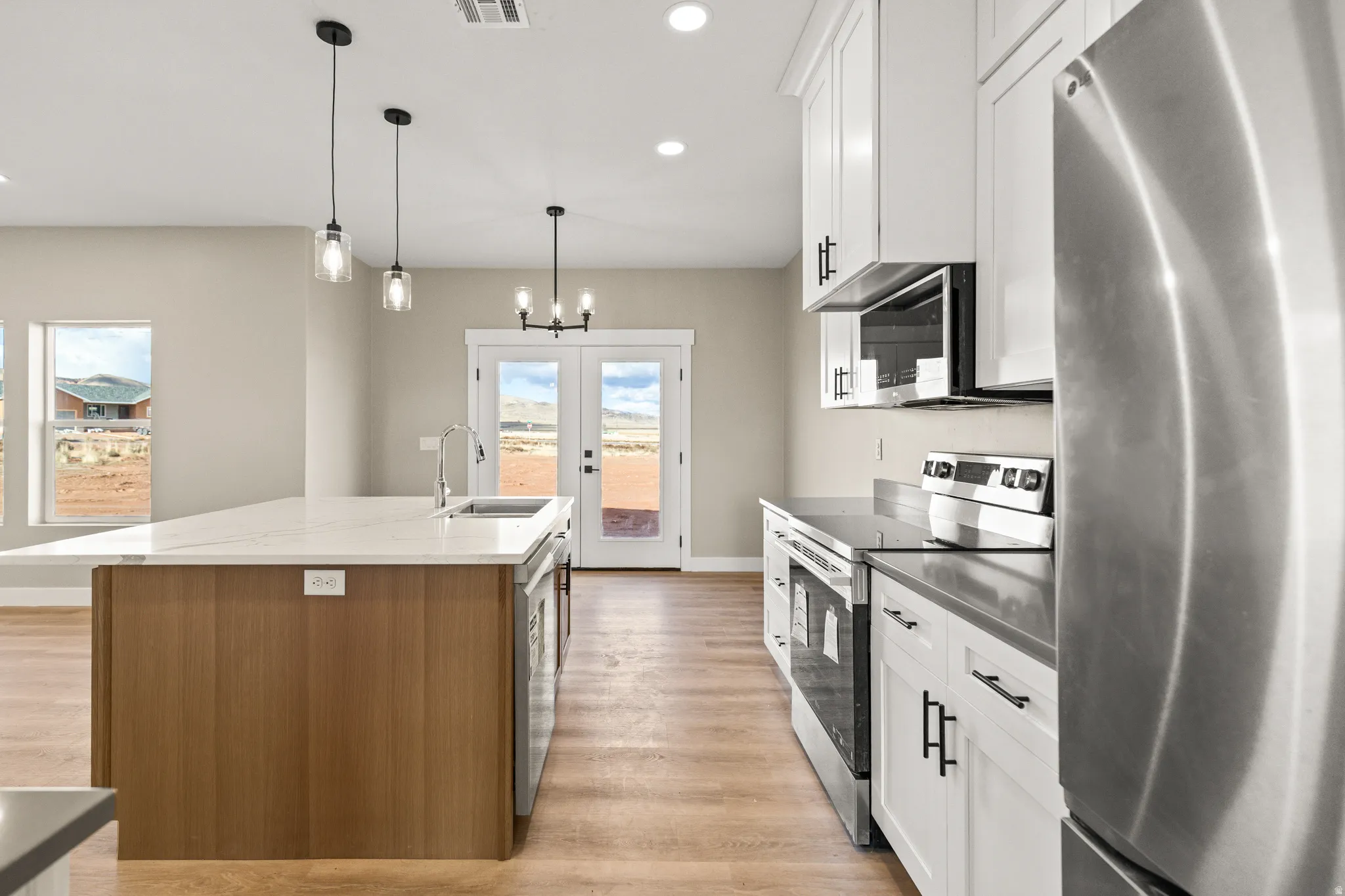 Kitchen with stainless steel appliances, white cabinets, french doors, pendant lighting, and a kitchen island with sink