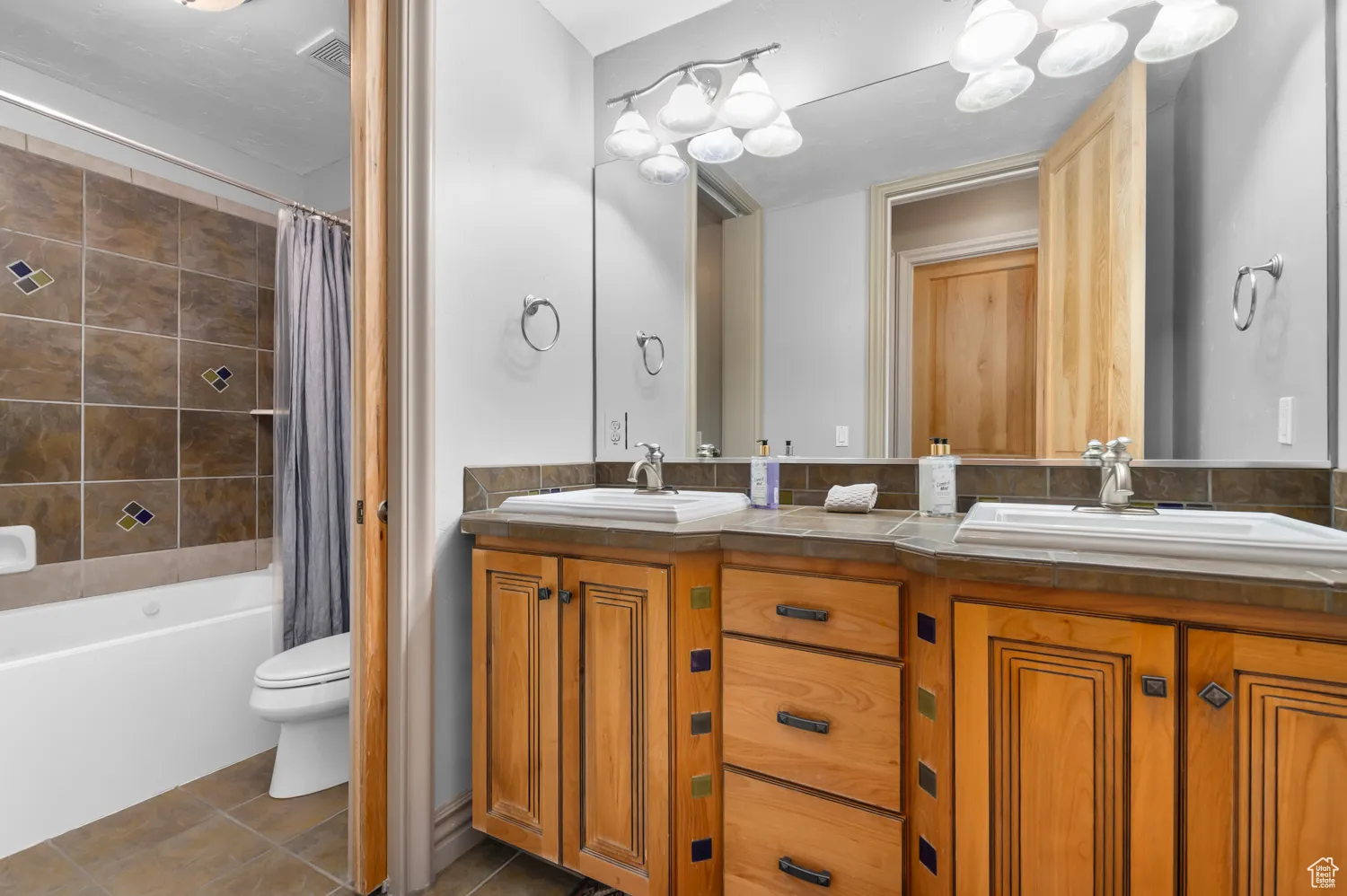 Full bathroom with double vanity, toilet, tile patterned flooring, and shower / bath combo