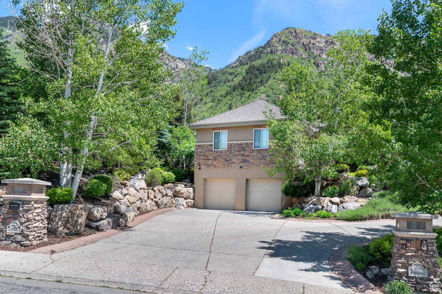 View of property hidden behind natural elements with stucco siding, concrete driveway, a mountain view, a garage, and stone siding