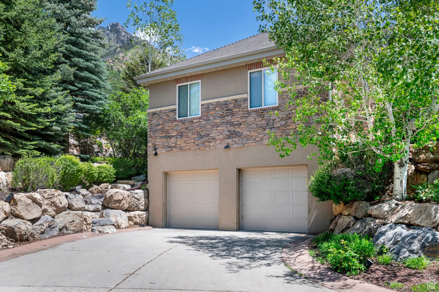 View of side of property featuring stucco siding, concrete driveway, an attached garage, and stone siding
