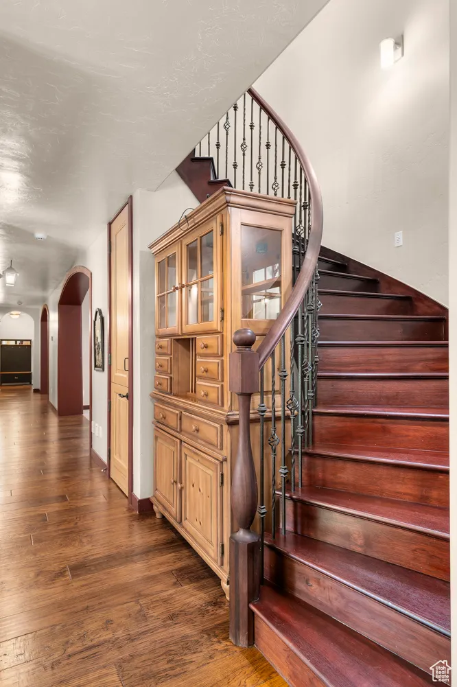 Staircase with arched walkways, wood finished floors, and baseboards