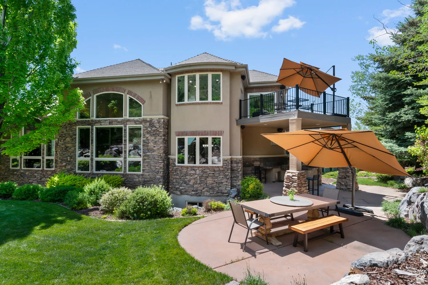 Rear view of house featuring a balcony, stucco siding, a patio area, stone siding, and a yard
