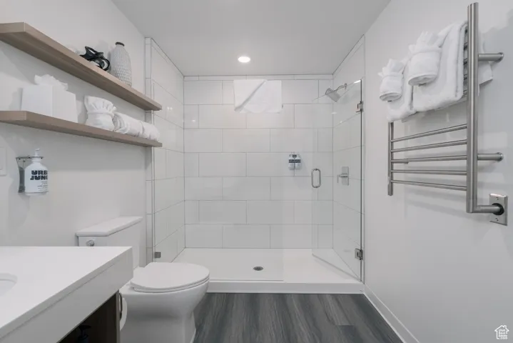Bathroom with radiator, toilet, a stall shower, wood finished floors, and vanity