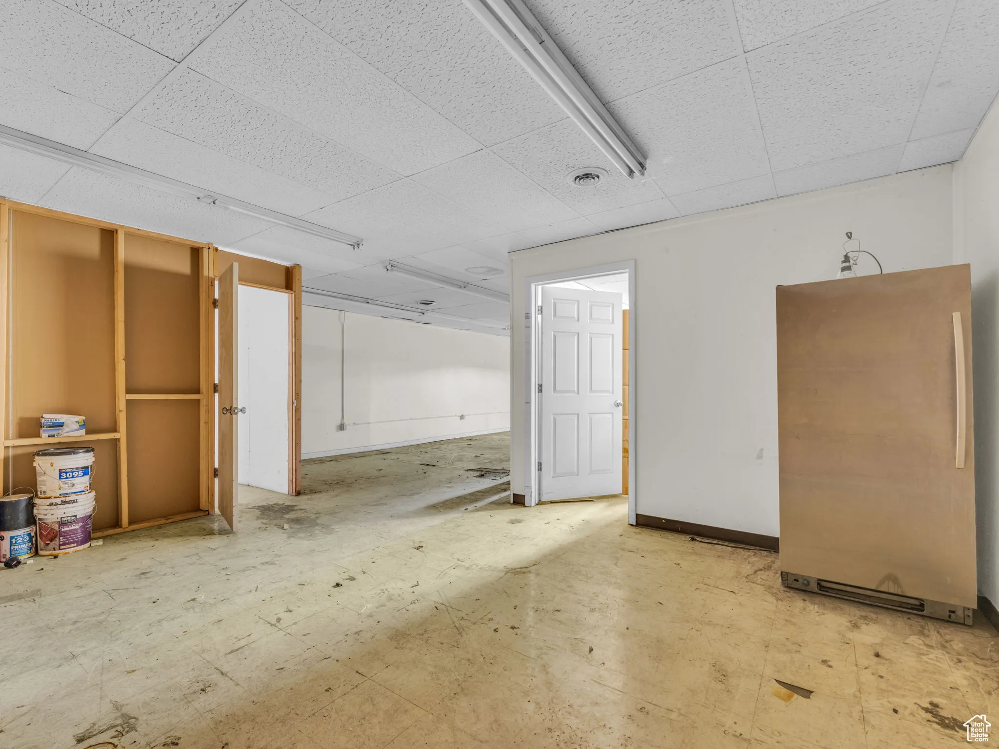 Basement featuring freestanding refrigerator, a drop ceiling, and baseboards