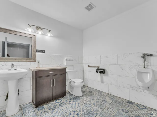 Bathroom with tile walls, toilet, a wainscoted wall, and a sink