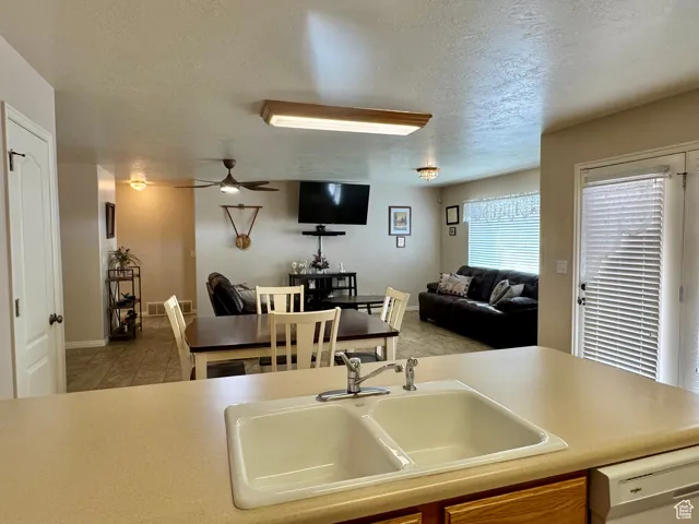 Kitchen with a sink, dishwasher, a textured ceiling, ceiling fan, and open floor plan
