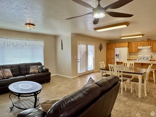 Living area featuring a textured ceiling, ceiling fan, baseboards, and light tile patterned flooring