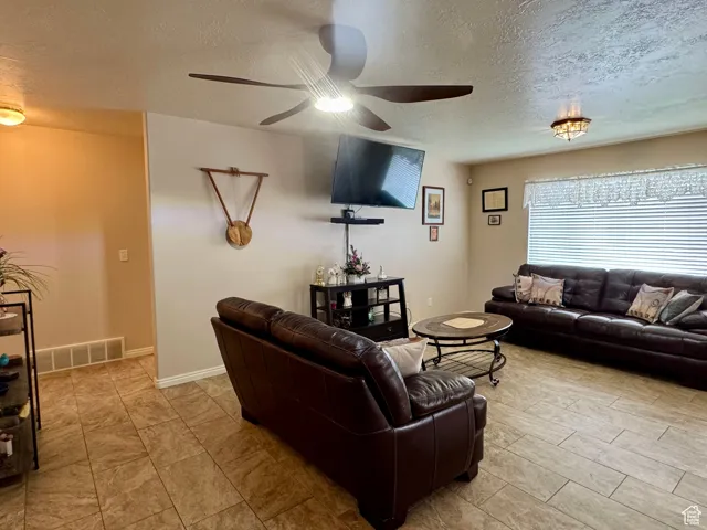 Living area with ceiling fan, a textured ceiling, and baseboards