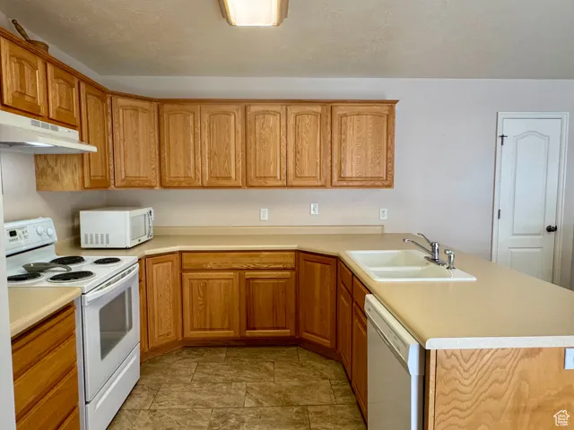 Kitchen with white appliances, a sink, under cabinet range hood, a peninsula, and light countertops